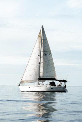 A sail boat floating on the water in calm waters.