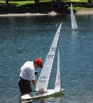 A man is standing on the water with his sailboat.